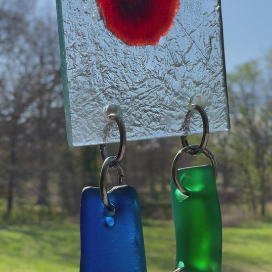 A Jupiter glass red spot glows through a clear textured glass square at the head of a chunky glass sun chain. There are 8 chunky pieces of glass  frosty clear, blues, greens. It’s 37.5” long, weighs about 5 pounds. 